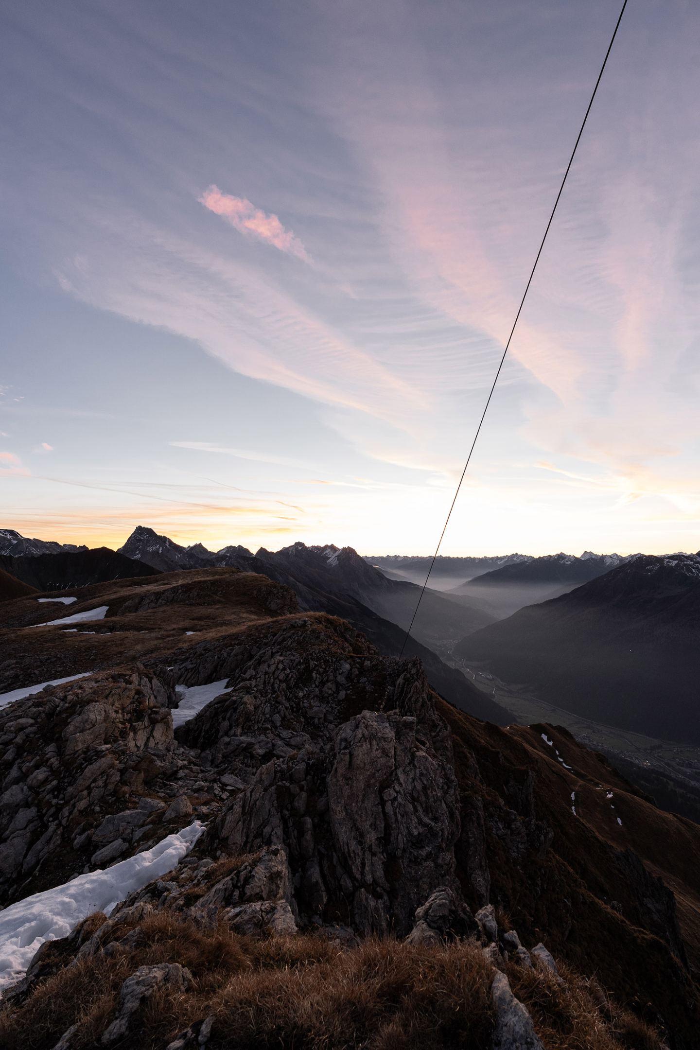 Sonnenaufgang am Berggrat mit felsigem Vordergrund und Pastellhimmel über dem Arlberg