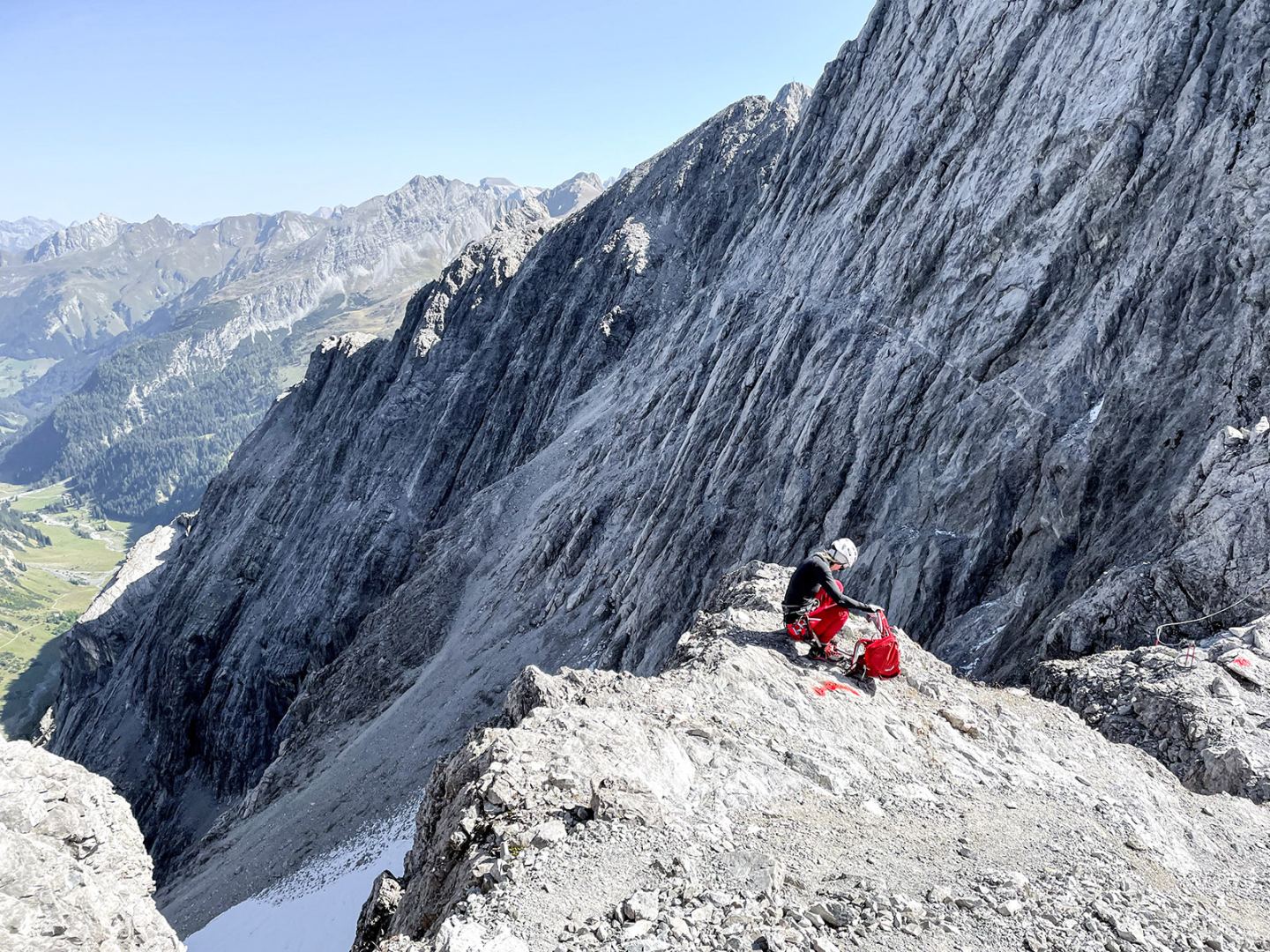Mountaineer resting on a rock ledge below a steep face on the Arlberg