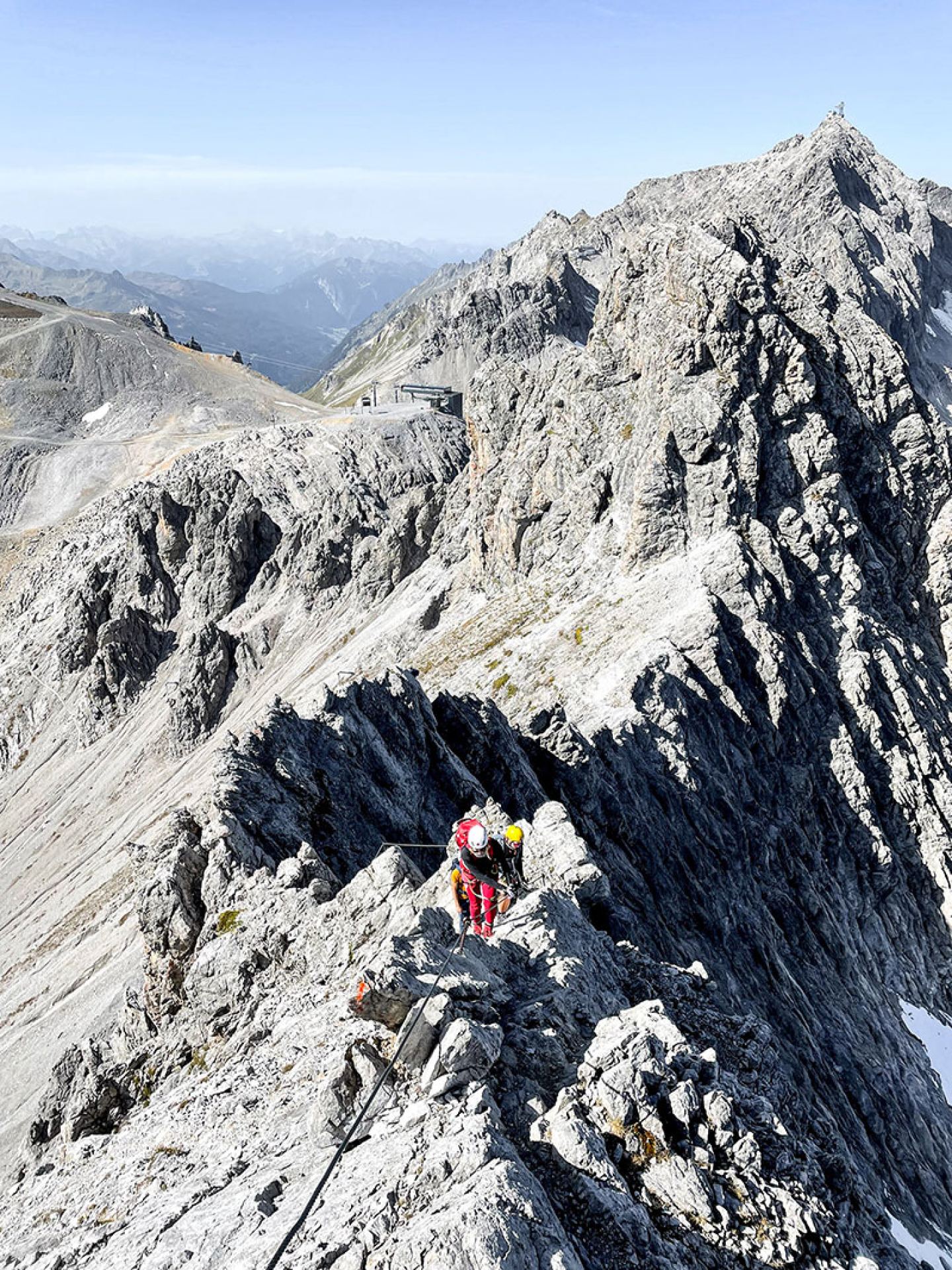 Climbers on the rocky ridge of the Arlberg via ferrata with summit panorama