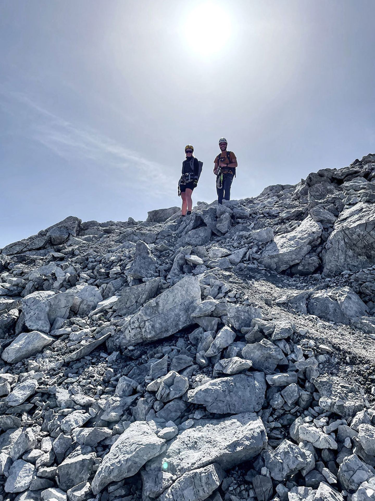 Two mountaineers on a rocky summit backlit by the sun on the Arlberg