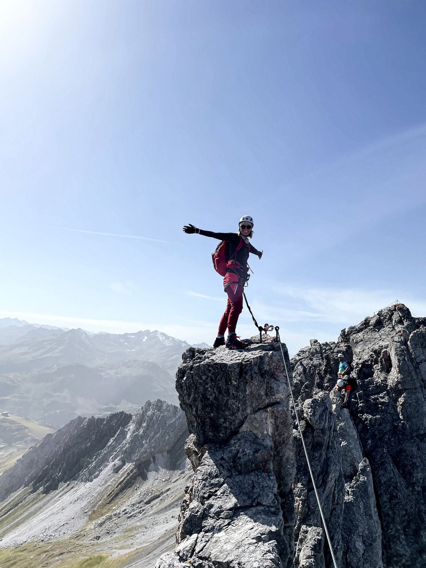 Mountaineer posing with outstretched arm on a summit pinnacle on the Arlberg