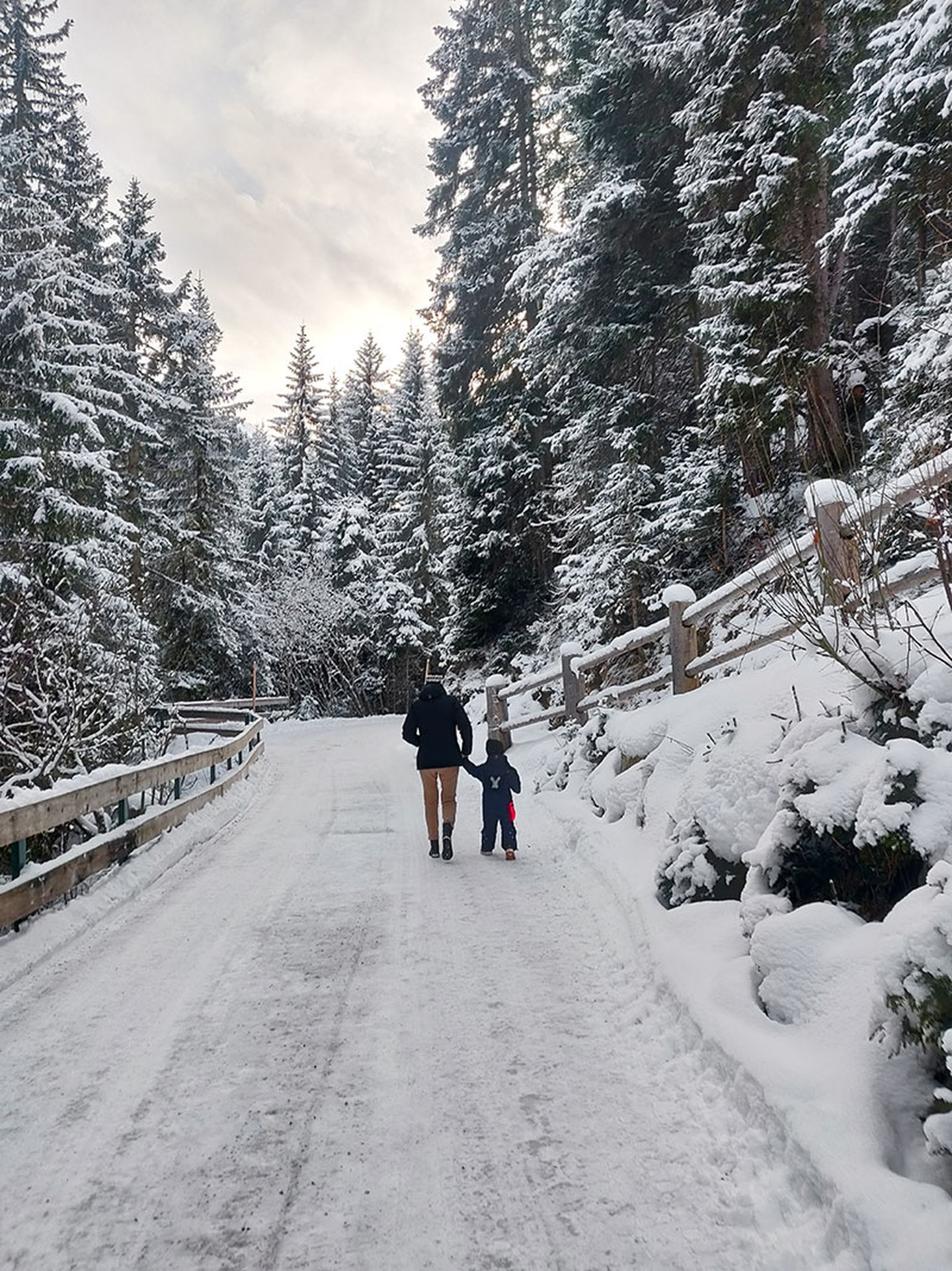 Winterwanderung von Eltern und Kind auf verschneitem Waldweg bei St. Anton am Arlberg