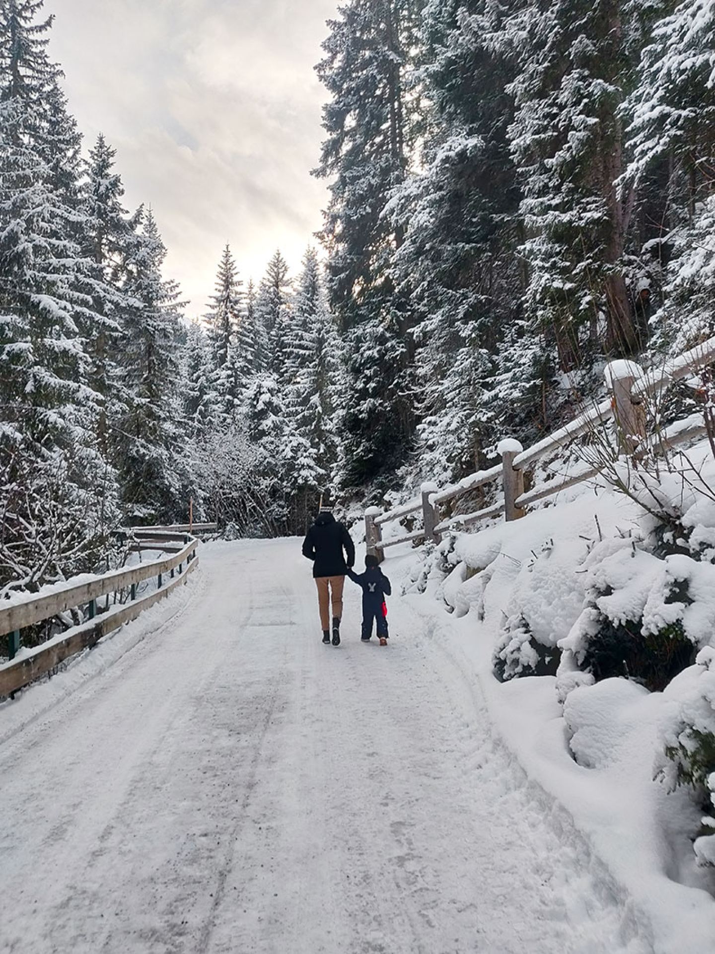 Winter walk of a parent and child on a snowy forest path near St. Anton am Arlberg