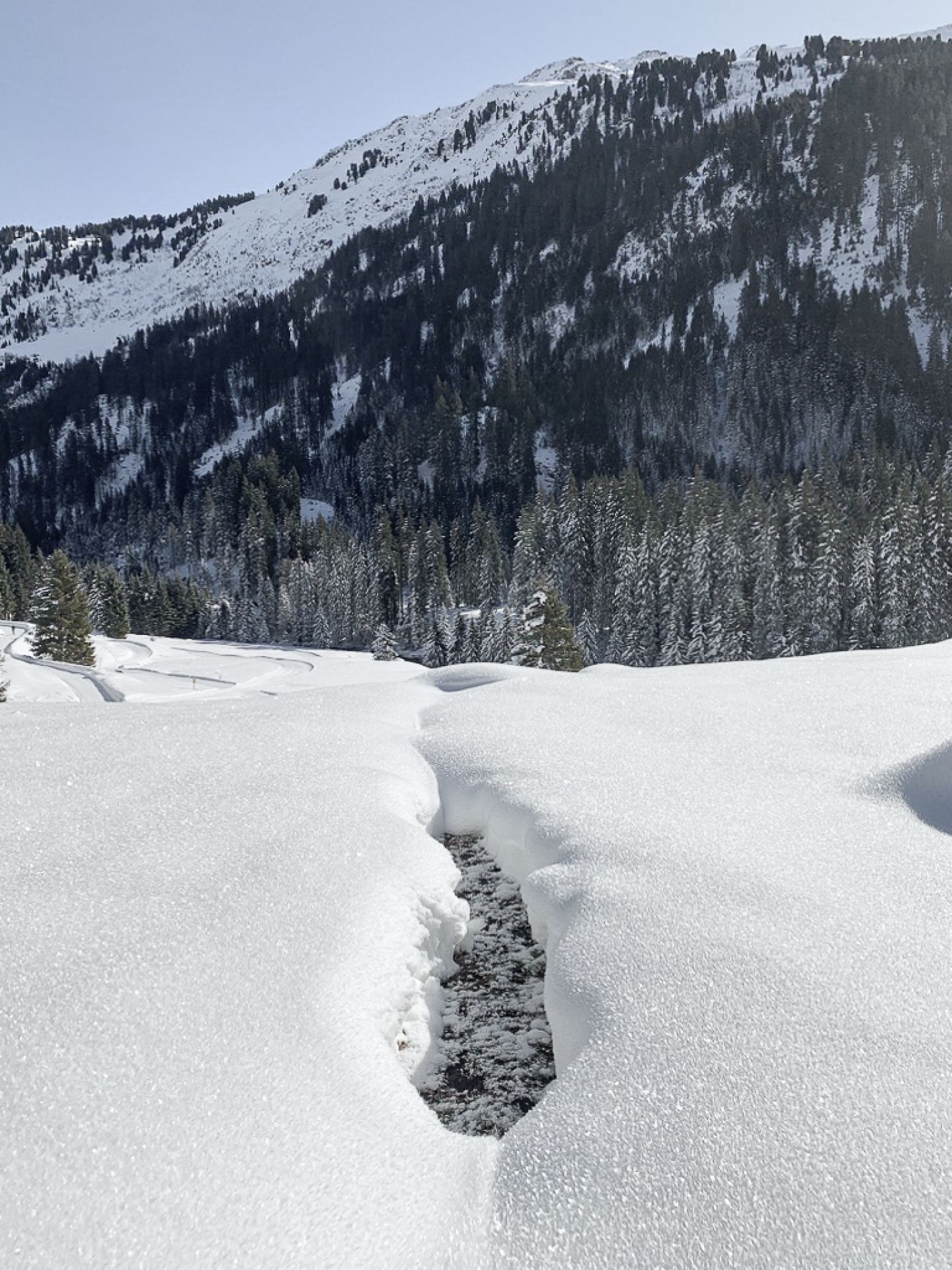 Winter landscape with a stream in deep snow below a forested slope on the Arlberg