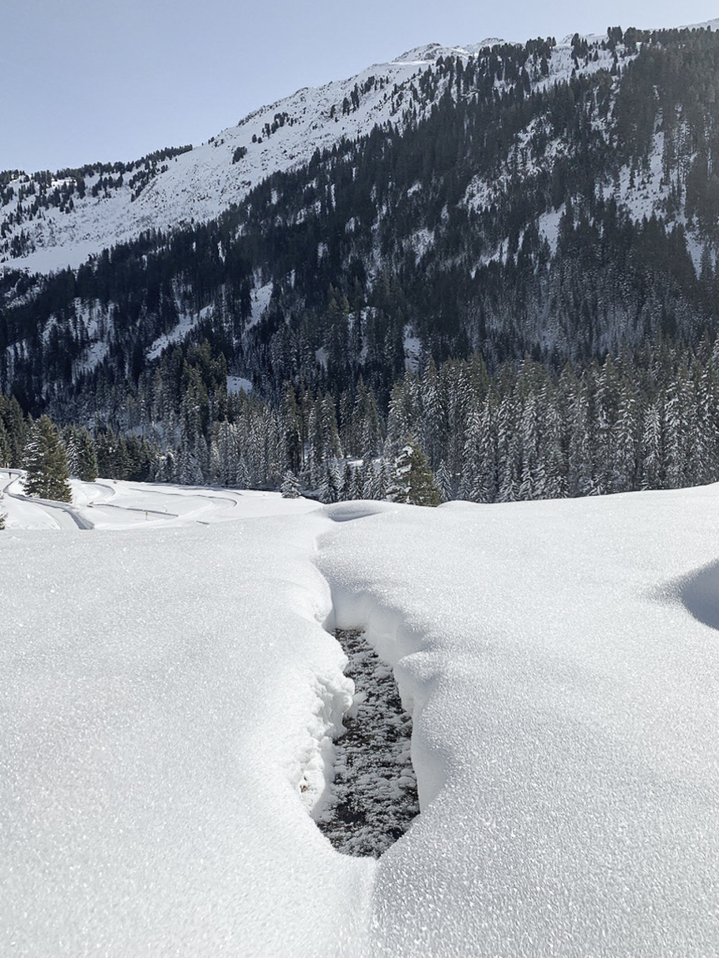 Winter landscape with a stream in deep snow below a forested slope on the Arlberg