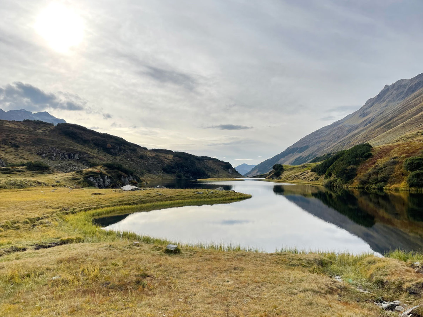 Bergsee Langer See mit spiegelnder Wasseroberfläche und grünem Ufer am Arlberg