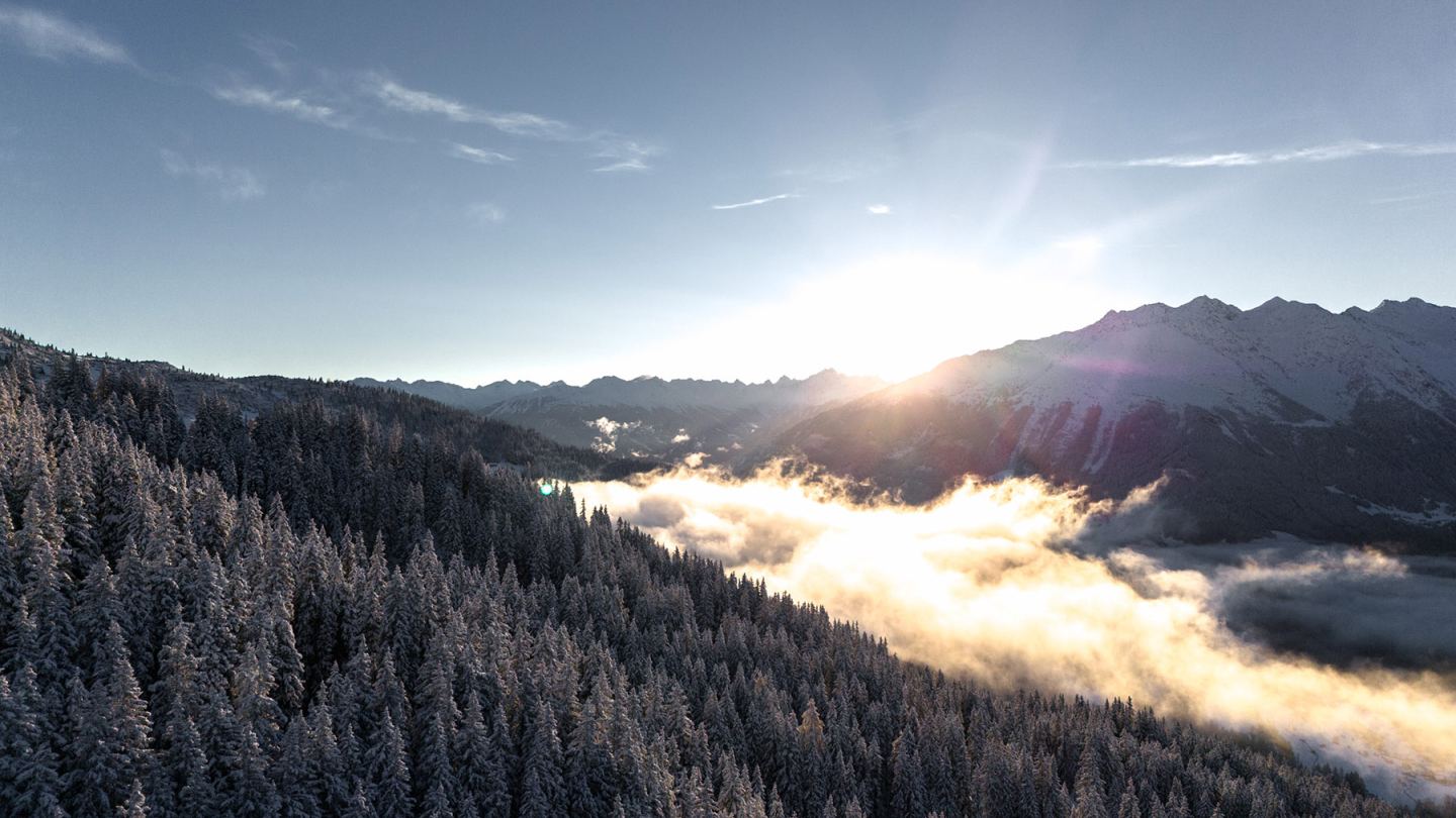 Drohnenaufnahme: Wintersonnenaufgang über verschneitem Wald und nebligem Tal am Arlberg