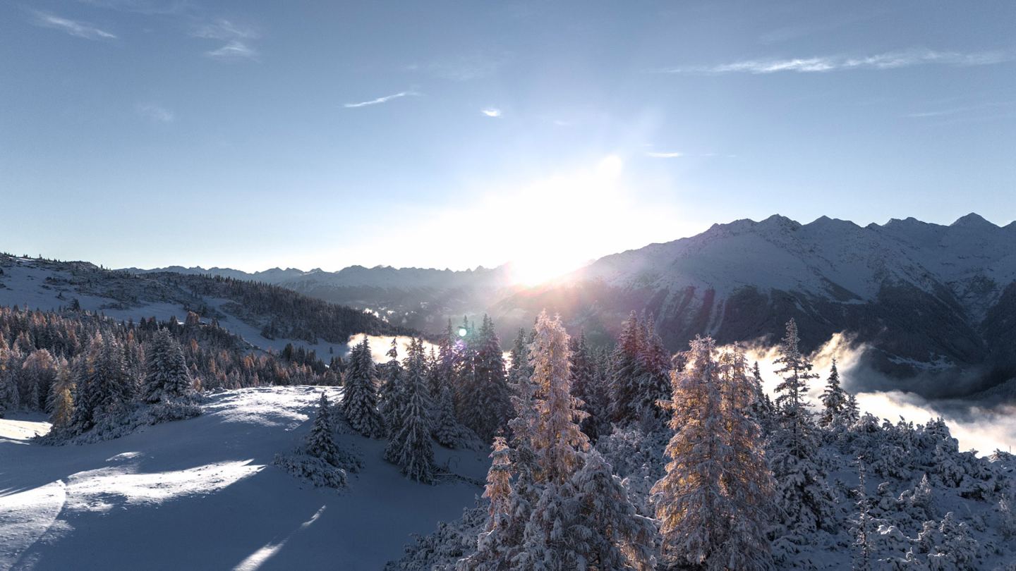 Drohnenaufnahme: Wintersonnenaufgang mit Sonnenstrahlen über verschneiten Bäumen am Arlberg