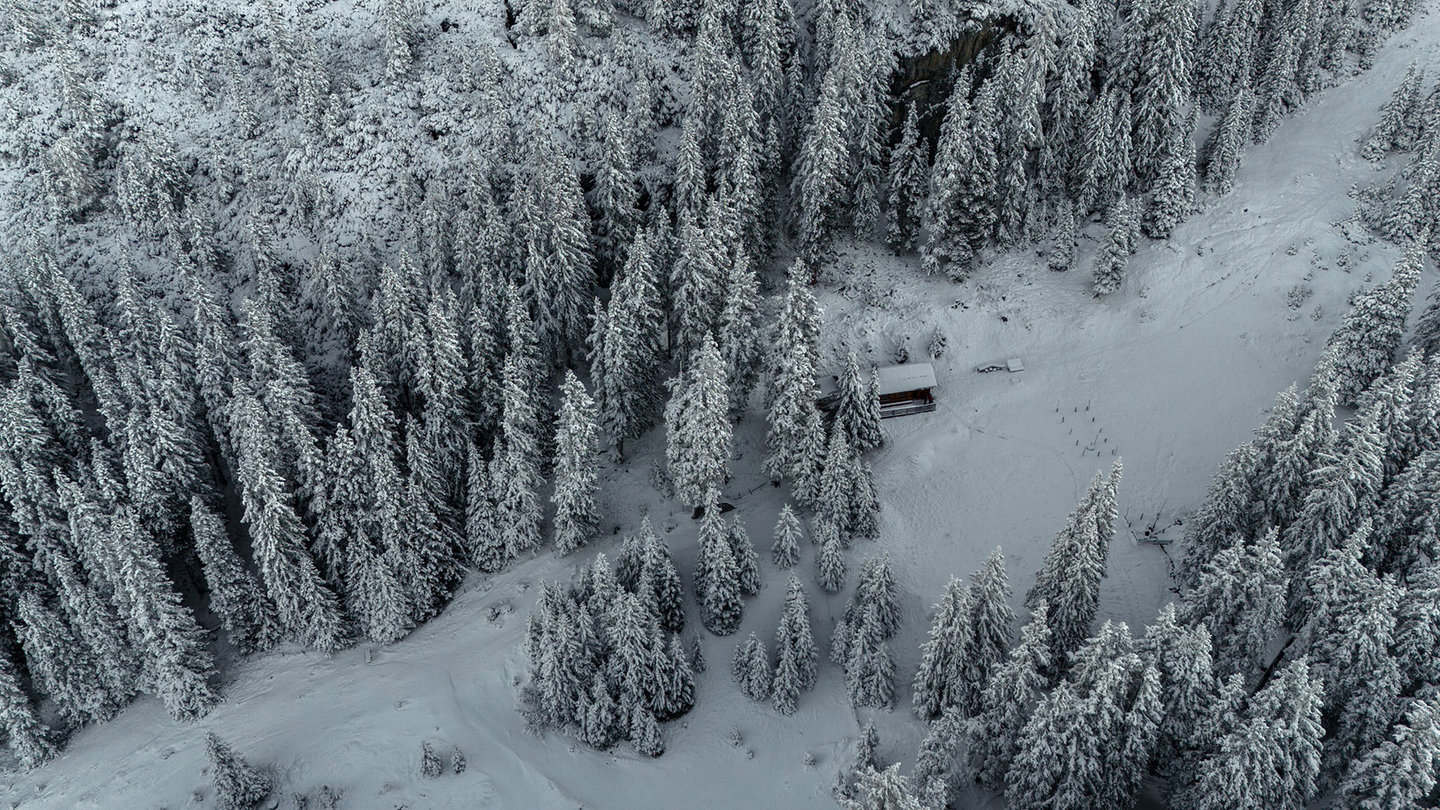 Drohnenaufnahme: kleine Hütte im tief verschneiten Fichtenwald von oben am Arlberg