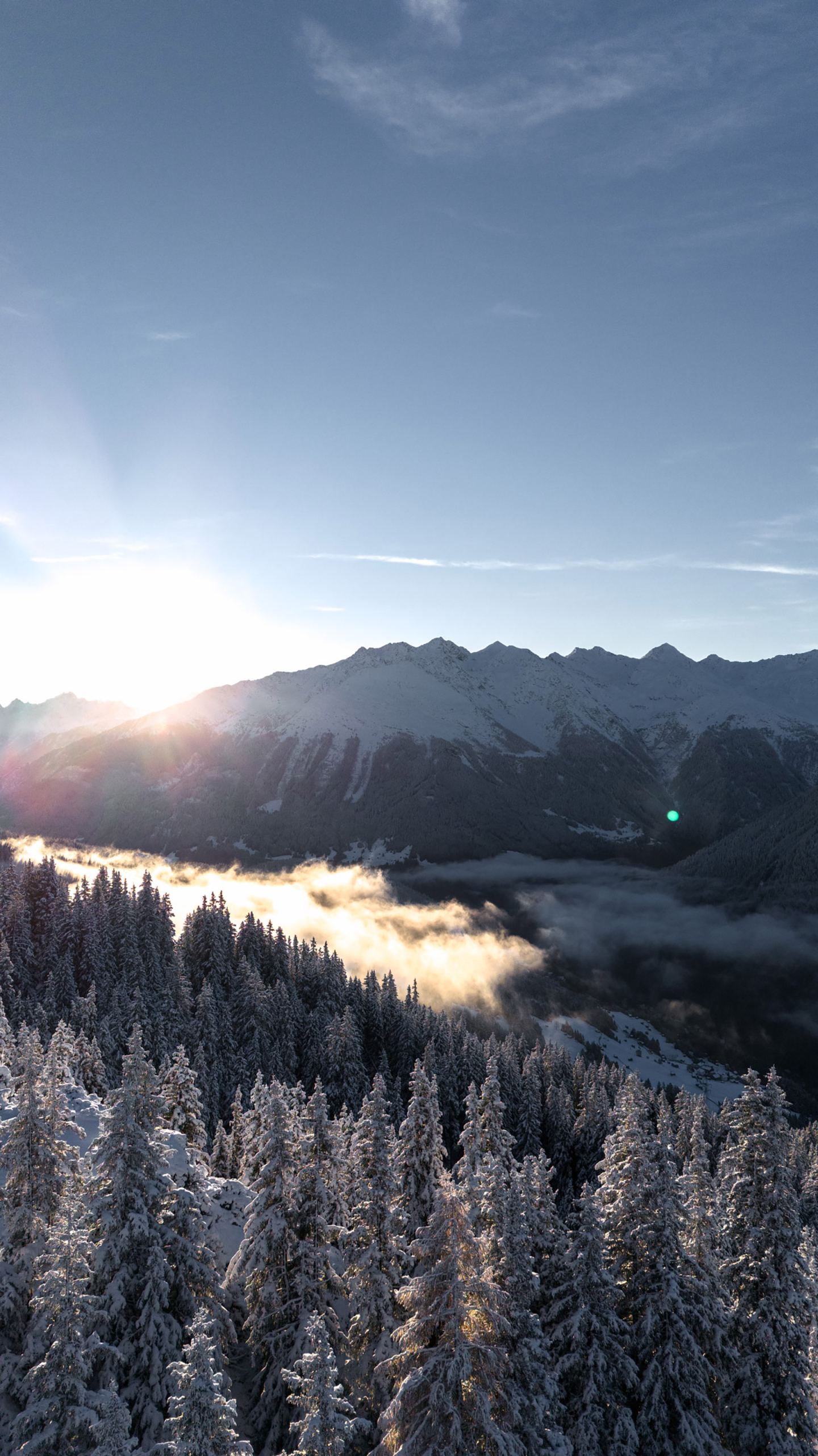 Drohnenaufnahme: Wintersonnenaufgang über verschneitem Wald und Tal mit Gipfeln am Arlberg