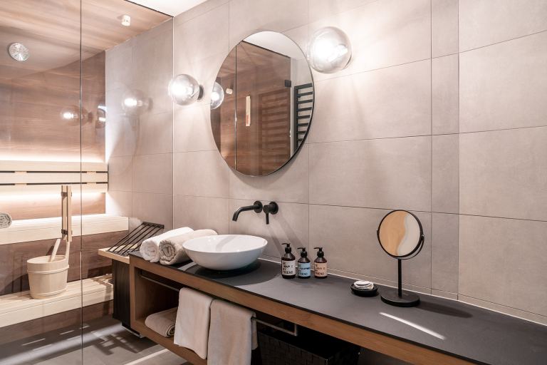 Modern bathroom with sauna, round mirror and vessel sink in the Omaela apartment
