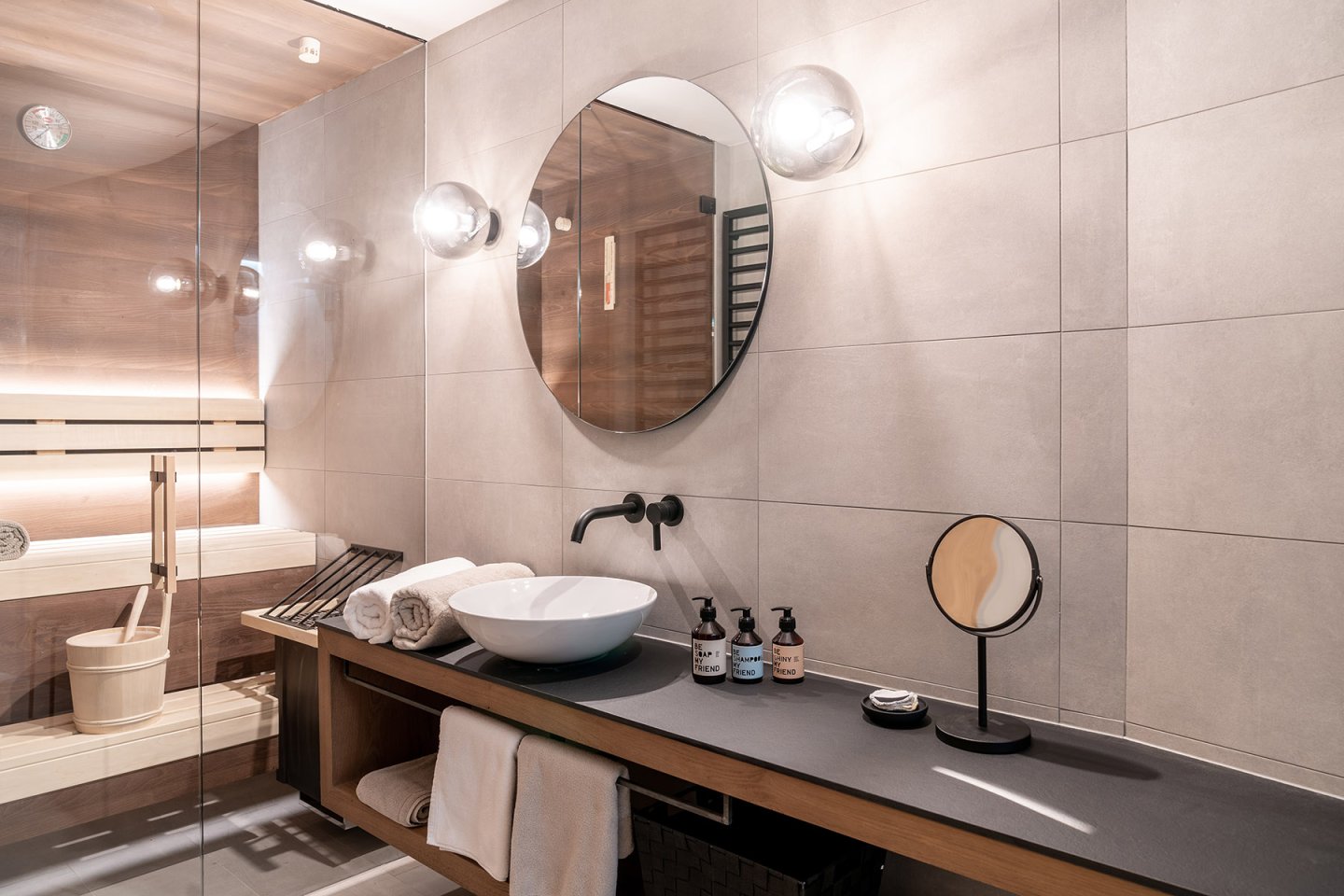 Modernes Badezimmer mit Sauna, rundem Spiegel und Aufsatzwaschbecken im Omaela Apartment