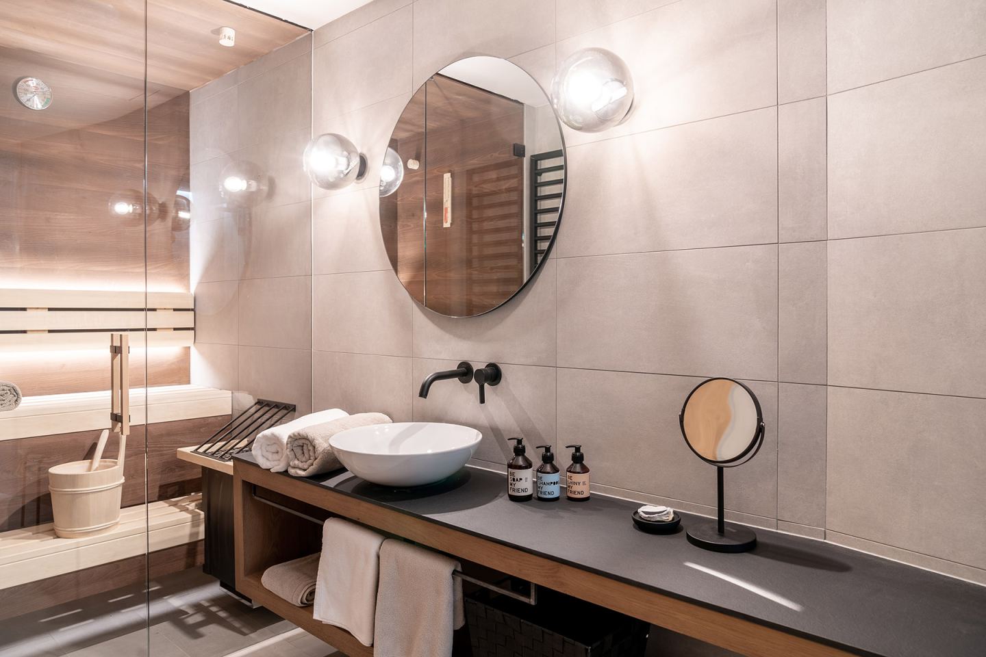 Modernes Badezimmer mit Sauna, rundem Spiegel und Aufsatzwaschbecken im Omaela Apartment