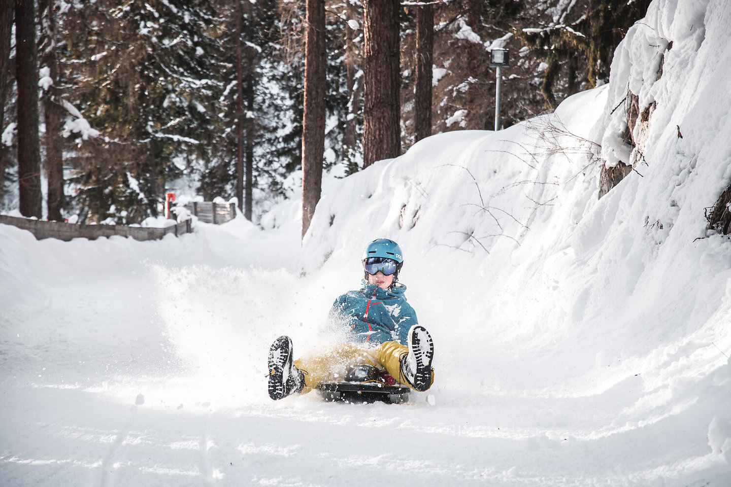 Kind rodelt mit Schwung auf einem verschneiten Waldweg in St. Anton am Arlberg
