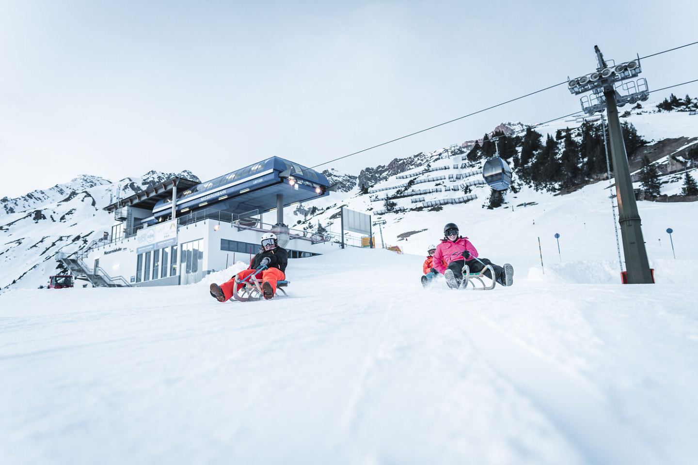 Zwei Personen rodeln im Schnee unterhalb der Bergstation am Arlberg