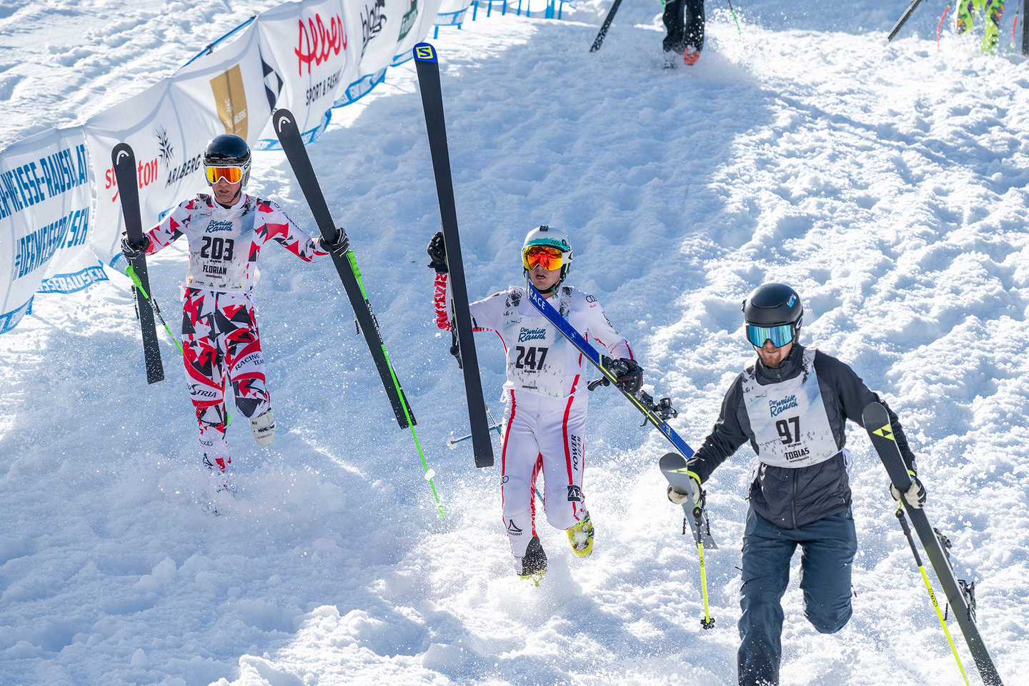 Skirennläufer laufen mit Ski bergauf beim Start des Weißen Rauschs 2025 in St. Anton am Arlberg