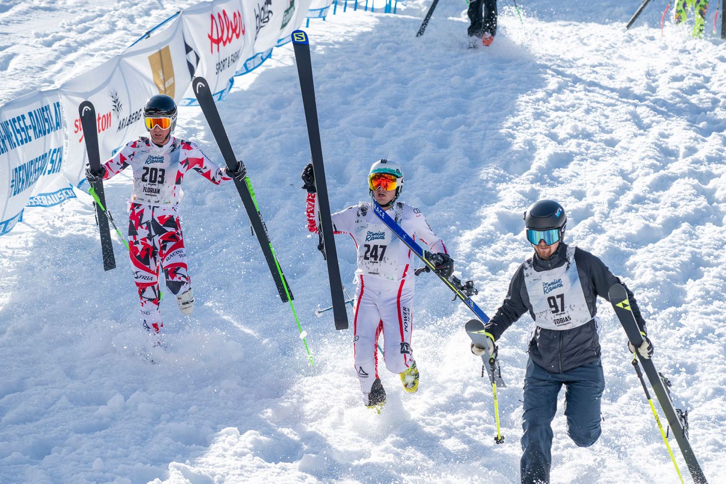 Skirennläufer laufen mit Ski bergauf beim Start des Weißen Rauschs 2025 in St. Anton am Arlberg